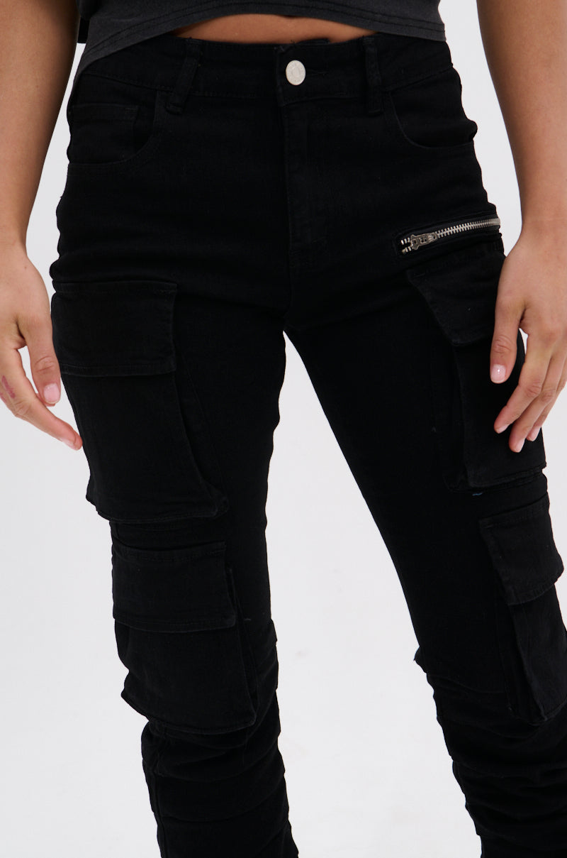 A person stands against a plain white background wearing the DOUBLE VISION VINTAGE WASH DENIM PANT, featuring a high-waisted fit, multiple pockets, and a visible zipper detail.
