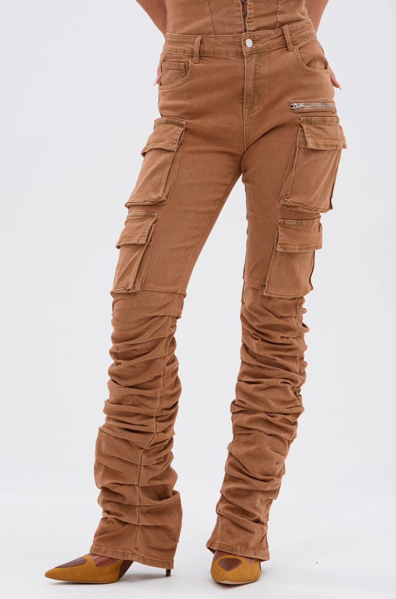 A person wears the IT GETS EASIER STACKED CARGO PANT IN MOCHA featuring multiple pockets and ruched legs, paired with pointed-toe brown shoes. Only the lower half is shown against a plain background. 2