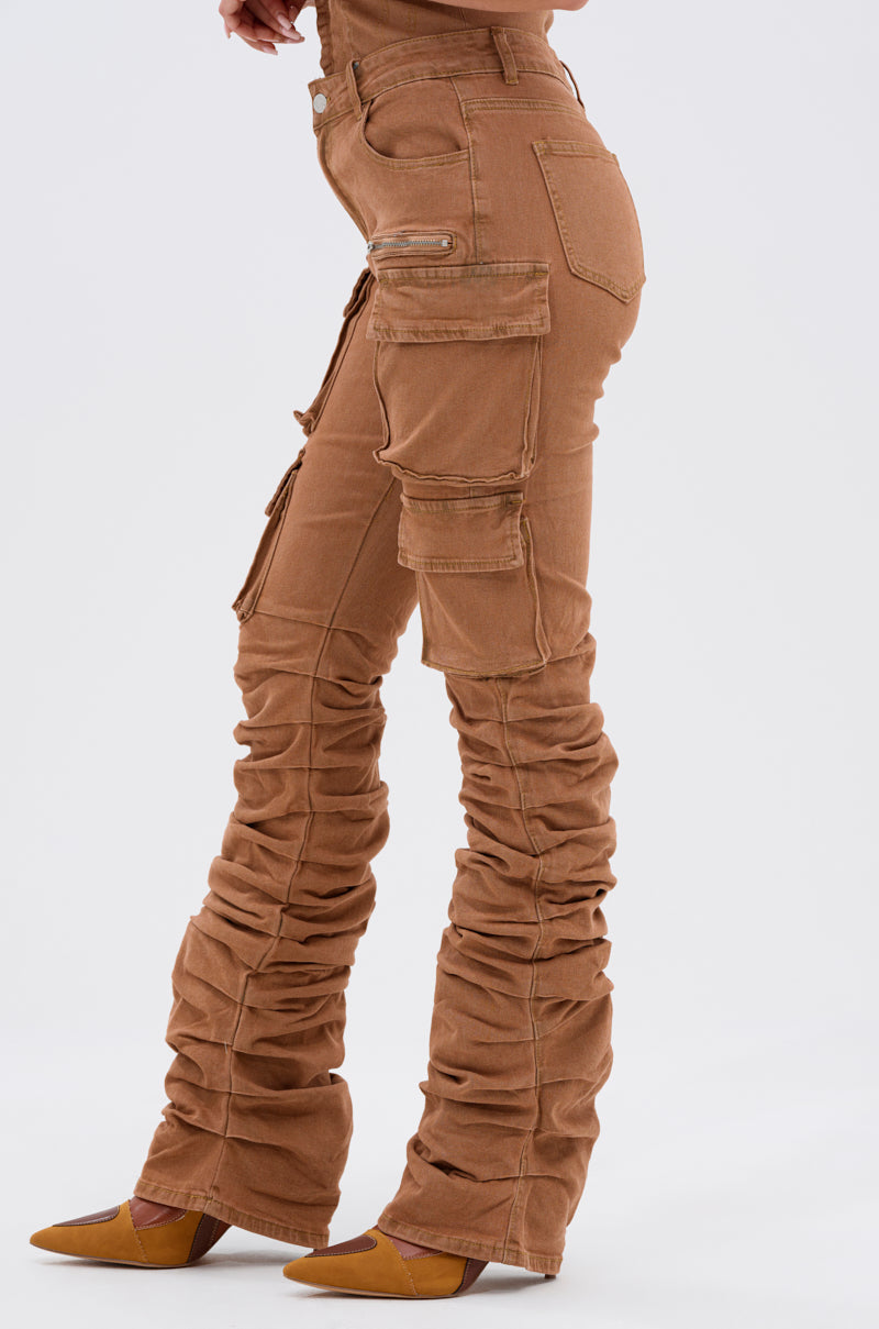 Model in the IT GETS EASIER STACKED CARGO PANT IN MOCHA with multiple pockets, styled with yellow pointed-toe heels, stands sideways against a plain light background. 3