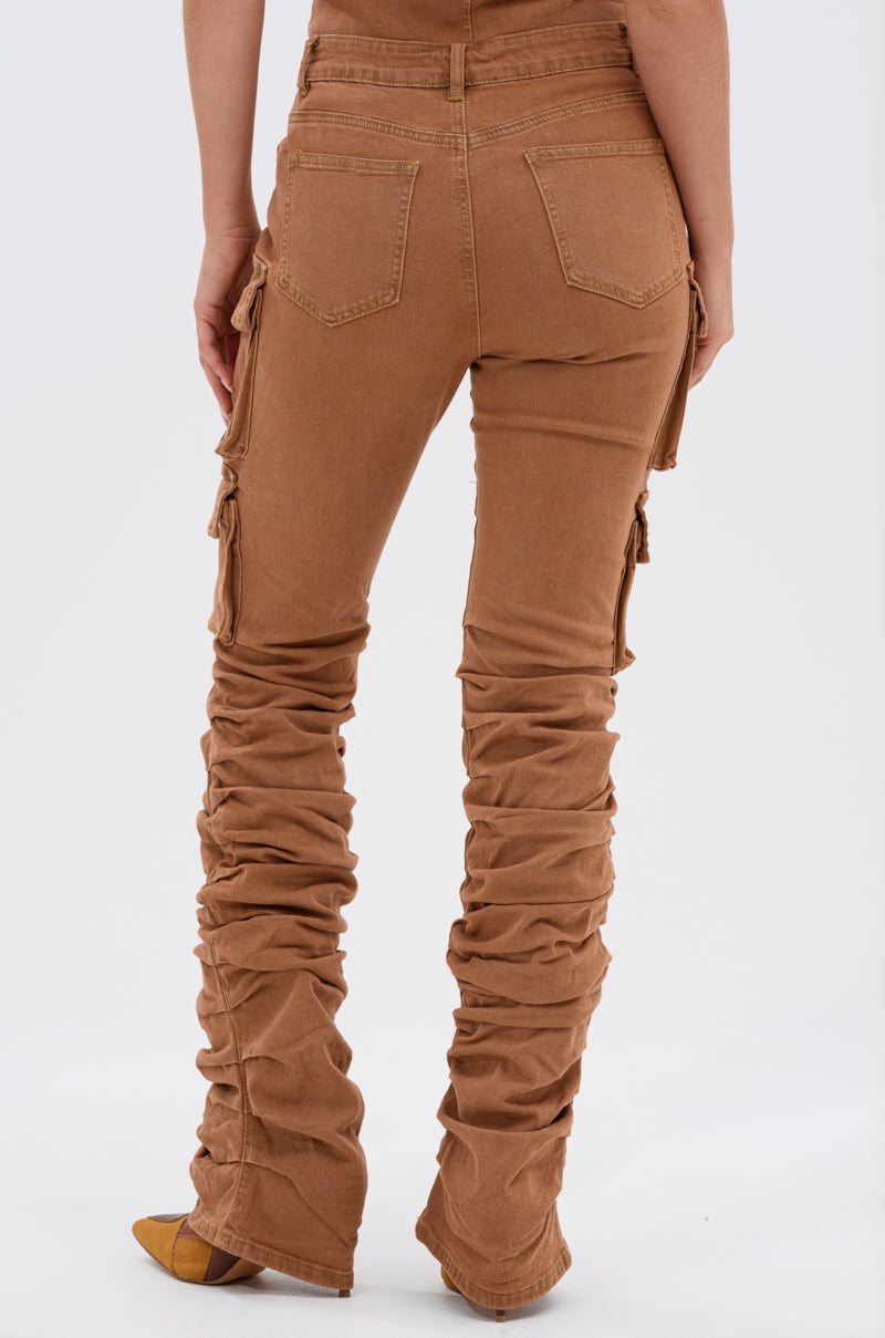 A person is wearing the IT GETS EASIER STACKED CARGO PANT IN MOCHA, featuring a high-rise fit, ruched legs, and side pockets. Only their lower back and legs are visible against a plain white background. 4