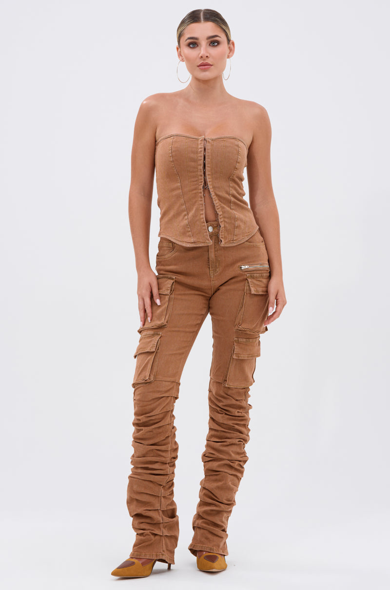 A woman faces forward in mocha IT GETS EASIER STACKED CARGO PANT with ruched detailing, a brown strapless button-up corset top, hoop earrings, and brown pointed-toe heels against a plain white background. 5