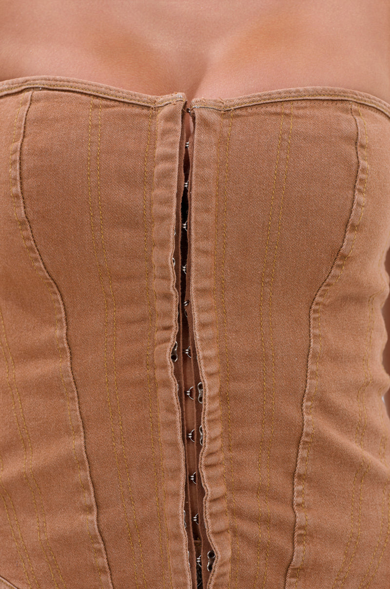 Close-up of a person wearing the IT GETS EASIER DENIM CORSET IN MOCHA, a strapless top with vertical stitching and a visible central hook-and-eye closure that highlights the upper chest and neckline. 6