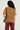 A person with long curly hair, wearing the FREEDOM OVERSIZED TEE in a grunge style featuring distressed holes, paired with maroon pants, is seen from the back. They are carrying a gray shoulder bag decorated with a gold metallic chain link.