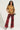 A person stands confidently in a FREEDOM OVERSIZED TEE, large sunglasses, and red distressed flared pants with pockets and grommets. They rock snakeskin boots and a handbag with a gold metallic chain link over their shoulder, exuding a grunge style vibe against the plain background.