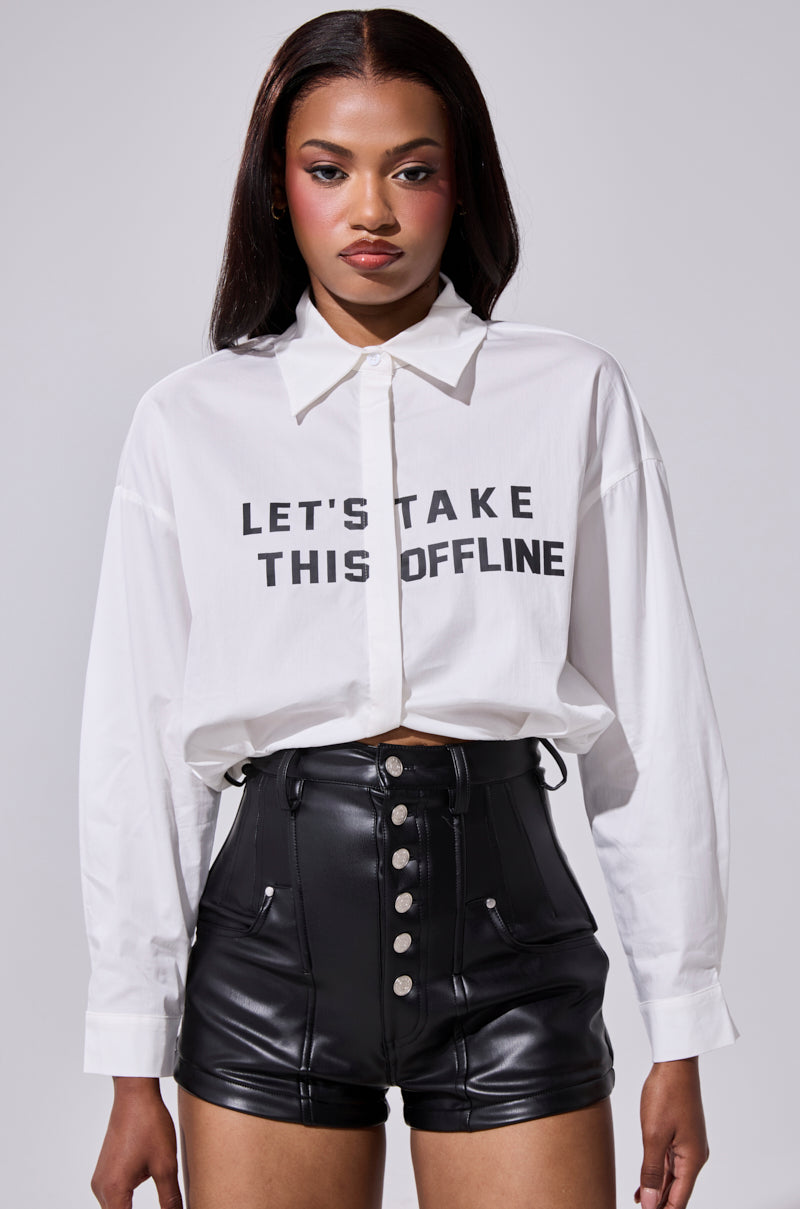 A woman with straight dark hair and a neutral expression faces forward, wearing the LETS TAKE IT OFFLINE BUTTON DOWN and high-waisted black leather shorts with buttons. 2