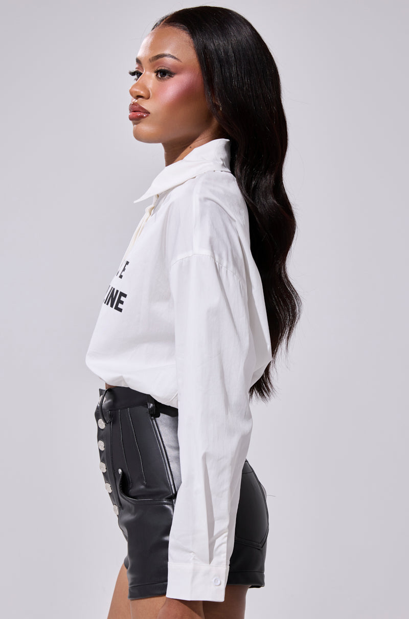 A woman with long, wavy dark hair stands in profile, wearing the LETS TAKE IT OFFLINE BUTTON DOWN shirt tucked into high-waisted black leather shorts with front buttons, creating a cyber chic look against a plain light gray background. 3