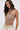 A woman wears the ICY GIRL RHINESTONE EMBELLISHED TOP IN GOLD, featuring crystal chains and intricate rhinestone details, paired with high-waisted cream pants against a plain light background—a stunning festival look.