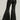 A person is seen from behind wearing the YES PLEASE FAUX LEATHER PANT, which features a black, high-rise fit with flared legs and gathered detailing at the waistband. The pants have a shiny finish as the individual stands against a neutral background.