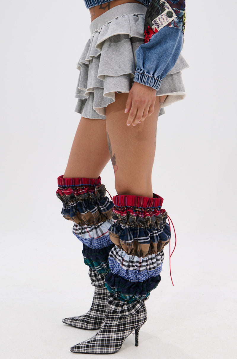 Someone wearing the ON THE MOVE RUFFLE SKORT in grey and tall, ruched, multicolored boots with plaid pointed toes poses against a plain white background.