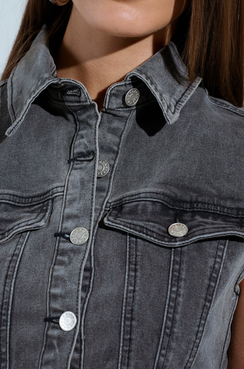 Close-up of a person wearing the MICHELLE DENIM MINI DRESS, featuring a gray denim fabric with a button front closure, metal buttons, and a collared neckline. The intricate stitching details are highlighted on the upper section against a light background.
