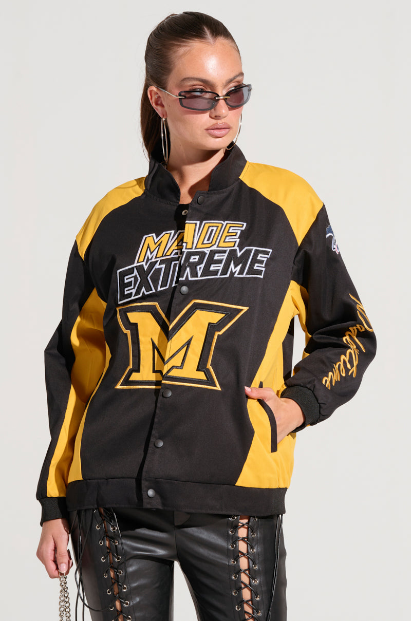 A person wearing the MADE EXTREME OVERSIZED BOMBER in black and yellow, showcasing "Made Extreme" text and a prominent "M" logo, along with embroidered sleeve graphics. They also sport sleek black leather pants, exuding style and confidence. 9