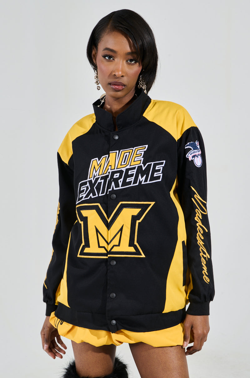 Wearing the MADE EXTREME OVERSIZED BOMBER with black and yellow colorblock, "Made Extreme" and a large "M" on the front, plus sleeve embroidery, they strike a pose against a neutral backdrop. 1