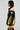 Someone with short, dark hair and earrings poses in profile against a plain backdrop, wearing the MADE EXTREME OVERSIZED BOMBER—a black and yellow varsity-style jacket featuring colorblock paneling and the phrase "Made Extreme.