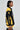 A woman is seen in profile sporting the MADE EXTREME OVERSIZED BOMBER, a black and yellow jacket with colorblock paneling and sports-inspired embroidered graphics. Her short hairstyle and large earrings complement the jacket's bold "M" and "Makestheme" design, enhancing its flair.