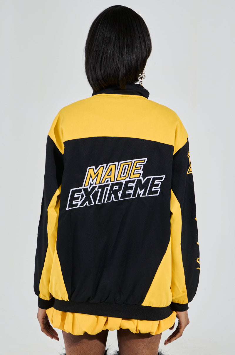 Someone is wearing a black and yellow MADE EXTREME OVERSIZED BOMBER, showcasing sports-inspired graphics and colorblock sleeves. The person faces away from the camera, emphasizing "Made Extreme" printed on the back of the jacket. 4