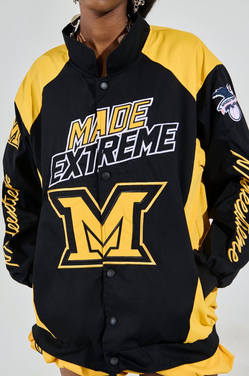 A person is wearing the MADE EXTREME OVERSIZED BOMBER in black and yellow, featuring a large "M" on the front and "Made Extreme" above it, with additional designs and text on the sleeves against a plain background. 8