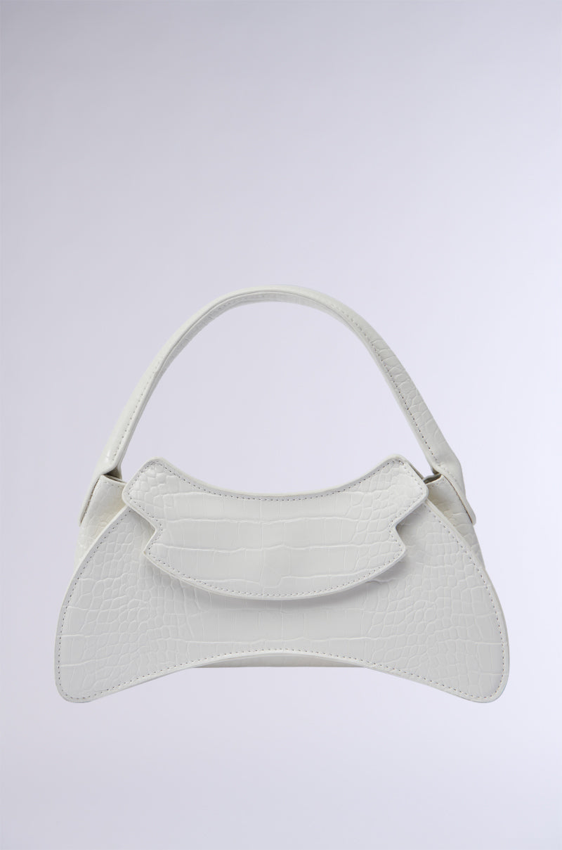 The CATWALK STATUS PURSE is a distinctive white handbag featuring a textured faux crocodile leather pattern. It showcases an unconventional hourglass silhouette, complete with a curved top flap and matching bottom. Designed with minimalism in mind, the purse includes a single carrying strap and is elegantly set against a plain, light gradient background.