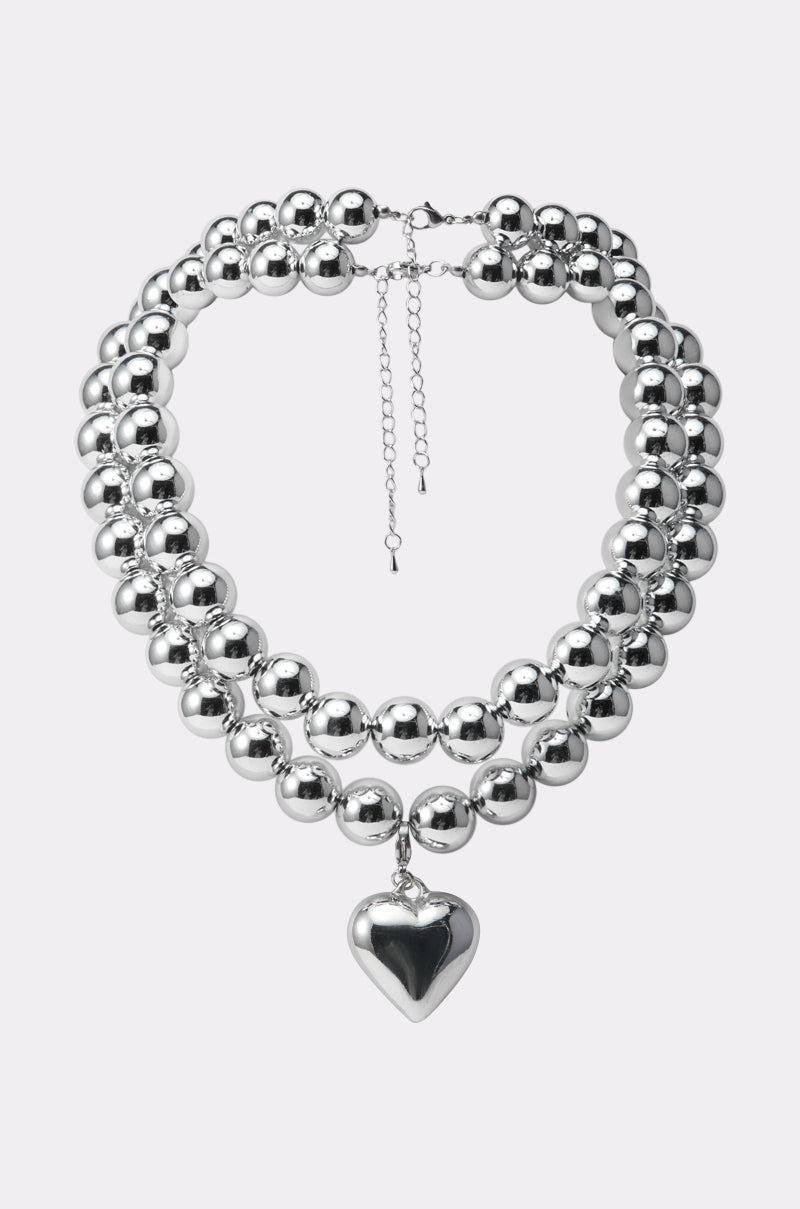 The Y2K DREAMIN SILVER NECKLACE features three silver beaded strands, a shiny finish, a bold puffy heart charm at the center, and an adjustable chain clasp for the perfect fit.