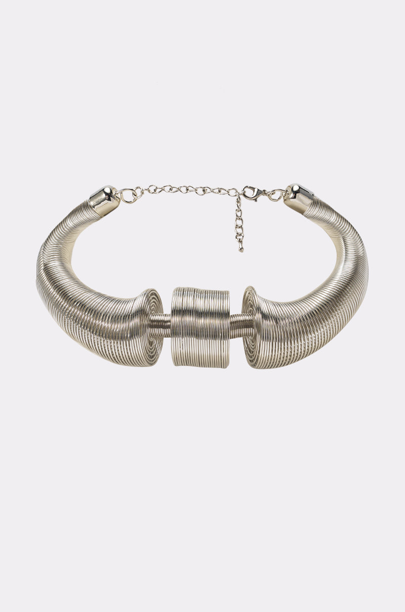 Introducing the SCULPTED COIL COLLAR IN SILVER: a statement silver choker necklace featuring a bold coiled wire design, highlighted by two prominent sculpted coils and a central cylindrical accent. The metallic collar includes a chain clasp for adjustable sizing, ensuring both comfort and style.