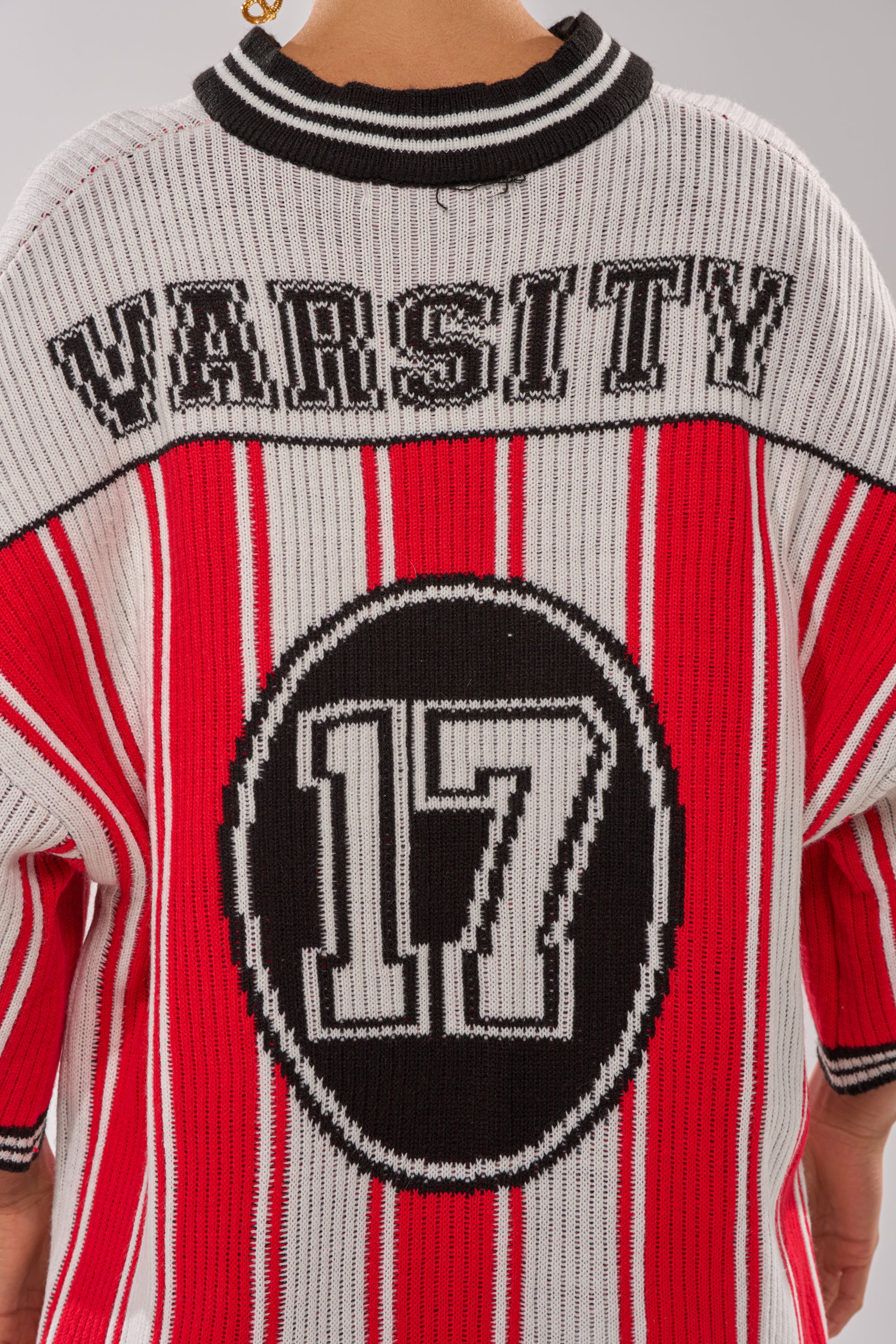 The THROW SUM MO KNIT JERSEY TOP’s back showcases bold black "VARSITY" text and a standout black circle with a white "17," all accented by red, white, and black stripes. 9