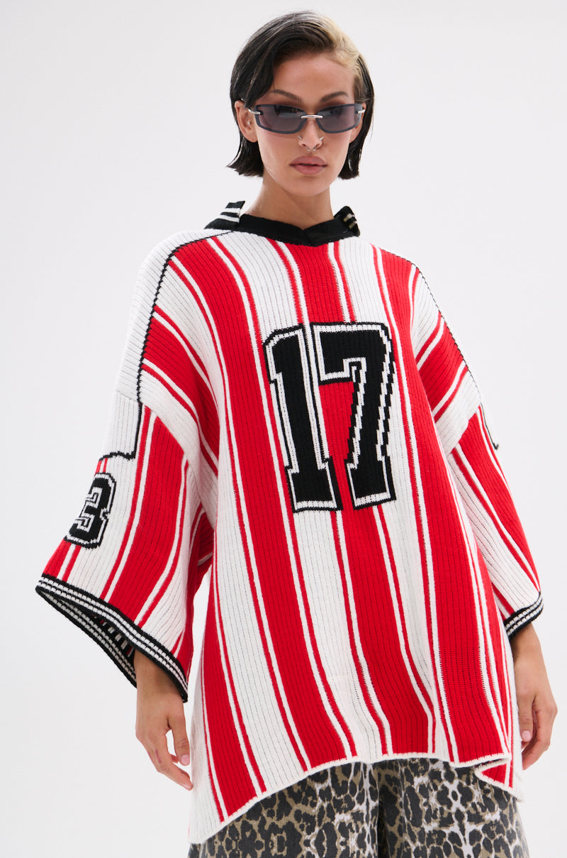 Wearing the THROW SUM MO KNIT JERSEY TOP—a varsity-inspired, red and white striped oversized sweater with “17” on the front and “93” on the sleeve—plus leopard print pants, sunglasses, and short dark hair against a plain background.