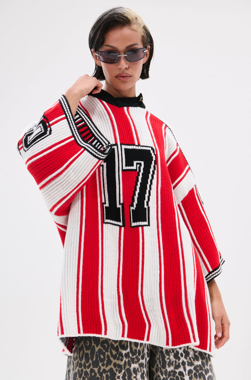 A person wears the THROW SUM MO KNIT JERSEY TOP, a varsity-inspired sweater with red and white stripes and the number 17, paired with a leopard print skirt, sunglasses, and a short hairstyle with a light blonde streak.