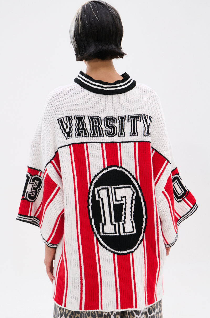 A person with short black and white hair is seen from the back wearing the THROW SUM MO KNIT JERSEY TOP—an oversized varsity-inspired sweater with red and white stripes, "VARSITY" on the shoulders, and numbers 17 and 13 on the back and sleeve.