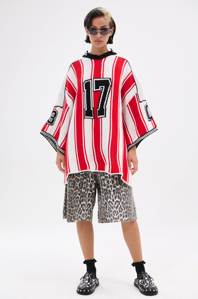 Someone stands against a plain white background wearing the THROW SUM MO KNIT JERSEY TOP—a sporty oversized jersey with red and white stripes and number 17—paired with leopard print shorts, black socks, studded black shoes, and sunglasses.