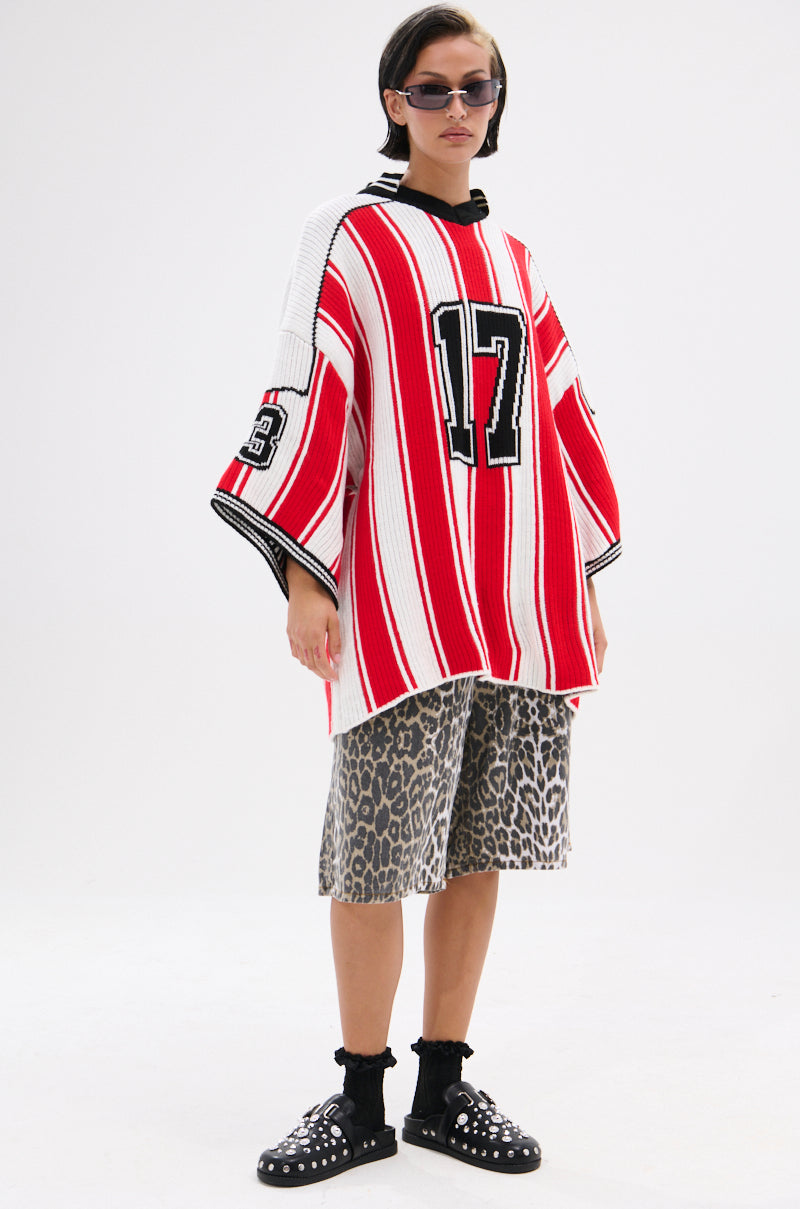 A person wearing sunglasses, leopard print shorts, black socks, black studded shoes, and the THROW SUM MO KNIT JERSEY TOP—a varsity-inspired red and white sweater with the number 17—stands against a plain white background.