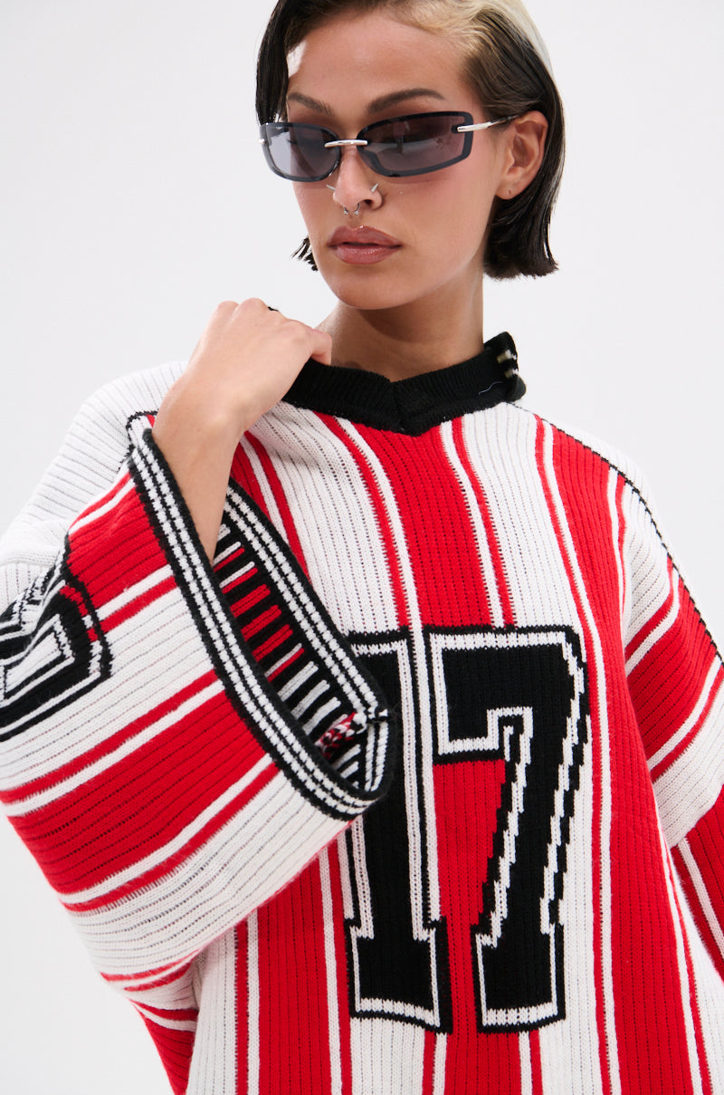 A person with short dark hair and sunglasses confidently wears the THROW SUM MO KNIT JERSEY TOP, a varsity-inspired sweater featuring red, white, and black stripes and the number 17 on the front.