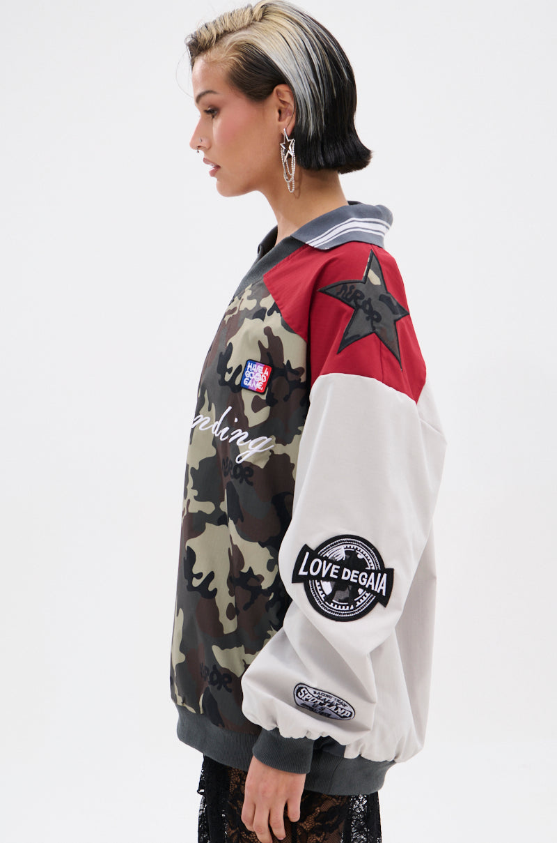 A person with short, two-toned hair stands sideways in front of a white background wearing the FLIP THE SWITCH PATCHWORK DETAILED JERSEY TOP—an oversized, relaxed silhouette with camo, red panels, and star patches.