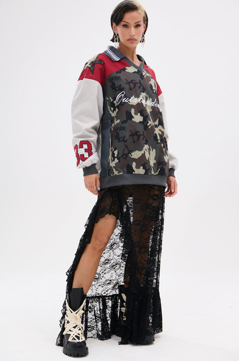 A woman stands confidently in the FLIP THE SWITCH PATCHWORK DETAILED JERSEY TOP with red and gray accents, styled over a long black sheer lace skirt. Chunky beige lace-up boots complete her look against a plain white background.
