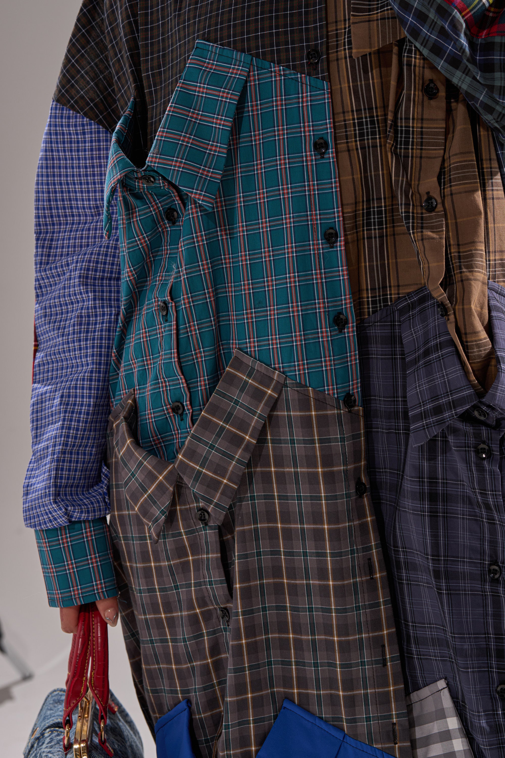 A close-up of the NOT YOUR BOYFRIENDS SHIRT DRESS, made from assorted plaid and checkered shirts in a patchwork design. A hand holding a red bag is partially visible on the left.