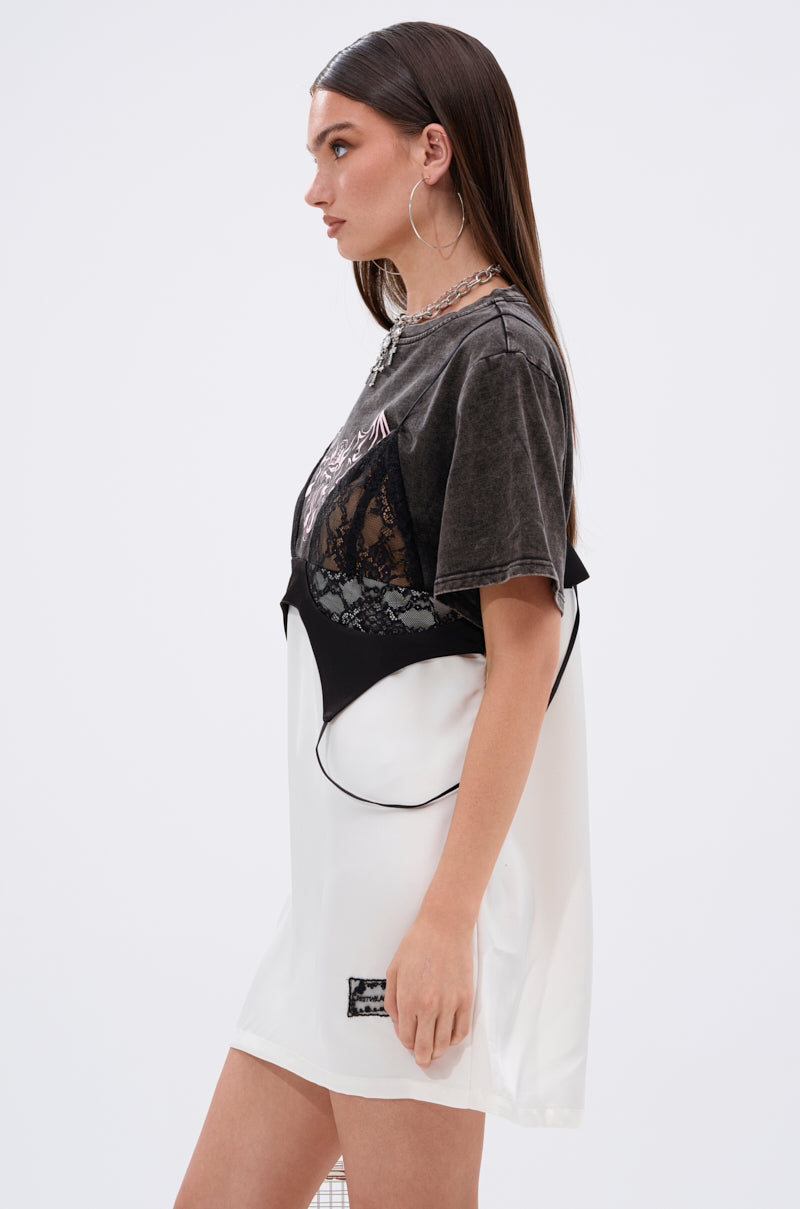 A woman in profile wears the QUIT STARING GRAPHIC TSHIRT DRESS in dark gray over a white slip dress with black lace paneling, accessorized with hoop earrings, layered necklaces, and straight brown hair.