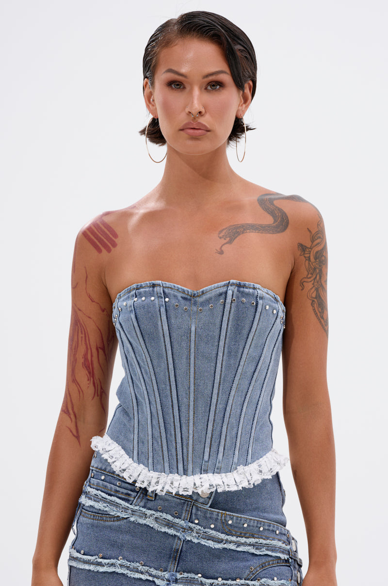 A person with short dark hair, hoop earrings, and visible tattoos models the DARLING LACE TRIM DENIM CORSET with a strapless sweetheart neckline and matching vintage blue wash skirt against a plain white background. 1