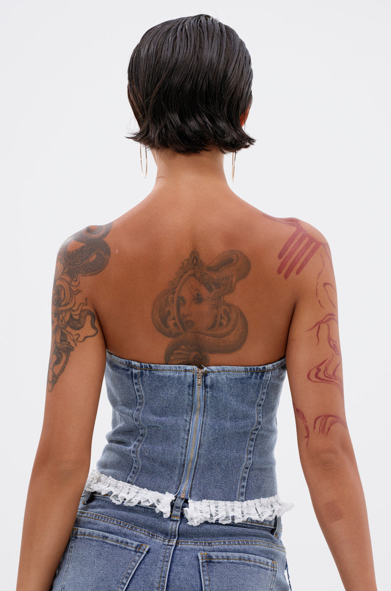A person with short dark hair and detailed tattoos wears the DARLING LACE TRIM DENIM CORSET in vintage blue. Seen from behind, the strapless top features lace trim, a sweetheart neckline, and a ruffled hem. 3