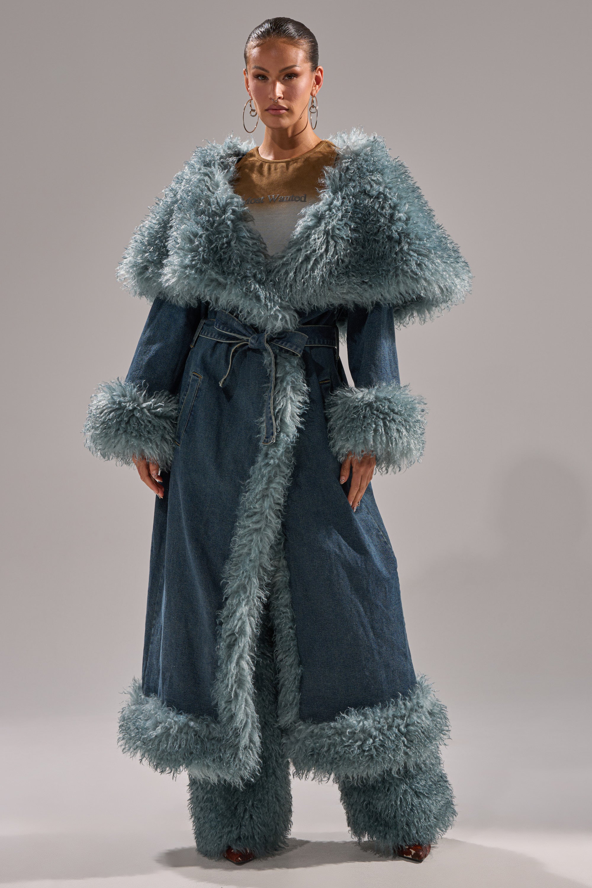 A woman faces forward in the MOXIE FUR TRIM DENIM TRENCH, featuring thick light blue fur on the collar, cuffs, hem, and opening. She wears matching pants against a plain gray background.