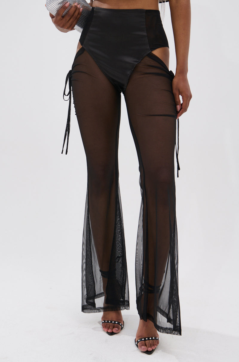 Someone models the DERRIA MESH FLARE LEGGING—high-waisted, black mesh flares with solid black briefs—styled with black heeled sandals and a clutch, standing against a plain white background. 2