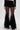 Wearing the CHLOE MESH FLARE MAXI SKIRT—high-waisted black shorts with sheer, pleated mesh maxi skirt overlays flaring at the ankles—paired with a black crop top and pointed black heels.
