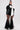 A woman stands in a black outfit featuring the CHLOE MESH FLARE MAXI SKIRT and a fitted top with puffed sleeves and a dramatic white bow at the neckline, paired with slicked-back hair, gold earrings, and black shoes.
