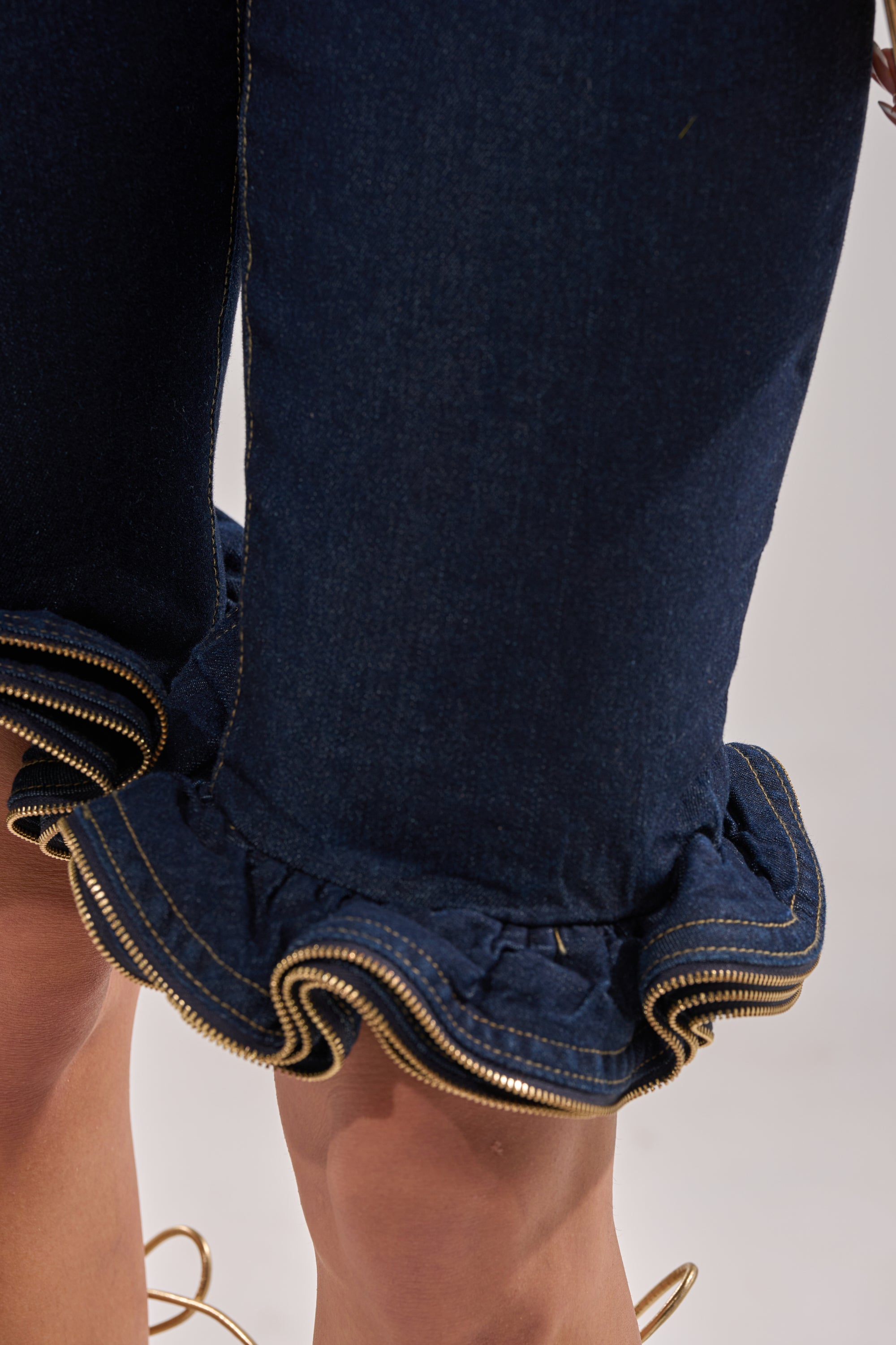Close-up of the SOMETHING DIFFERENT DENIM BERMUDA SHORT, featuring a high-rise fit, ruffle hems, and gold zipper details near the knees, worn by a standing model.