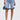 Wearing the LONDON BERMUDA SHORT in light blue with ruffled hems, paired with a matching blue handbag and blue fringe slide sandals. The upper body is not visible.