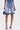 Wearing the LONDON BERMUDA SHORT in light blue with ruffled hems, paired with a matching blue handbag and blue fringe slide sandals. The upper body is not visible.