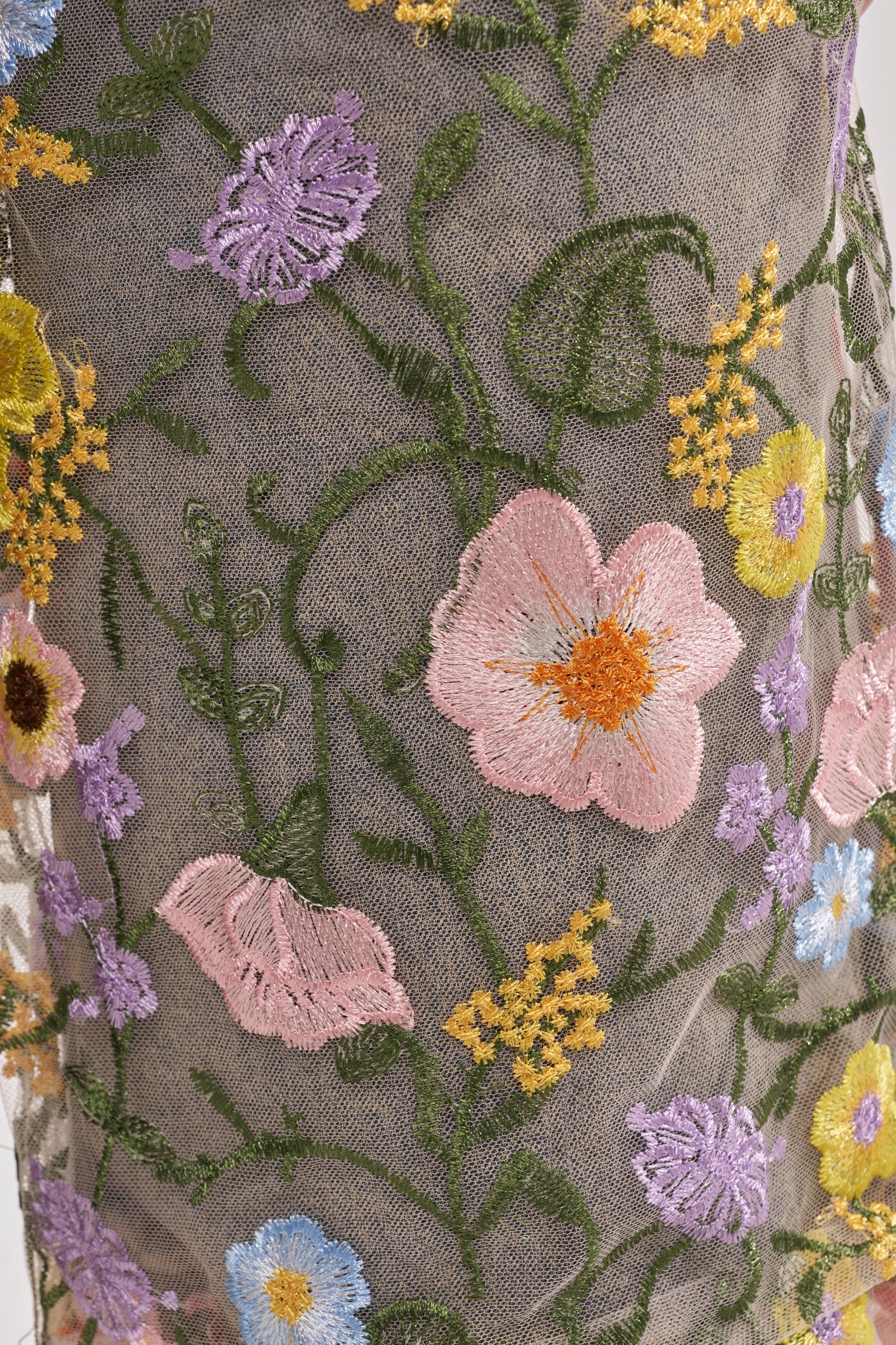 Close-up of the GARDEN PARTY STRETCH DENIM WITH FLORAL TULLE BERMUDA SHORTS featuring sheer fabric with a floral tulle overlay, embroidered blooms in pink, yellow, purple, and blue, plus green stems and leaves. 10