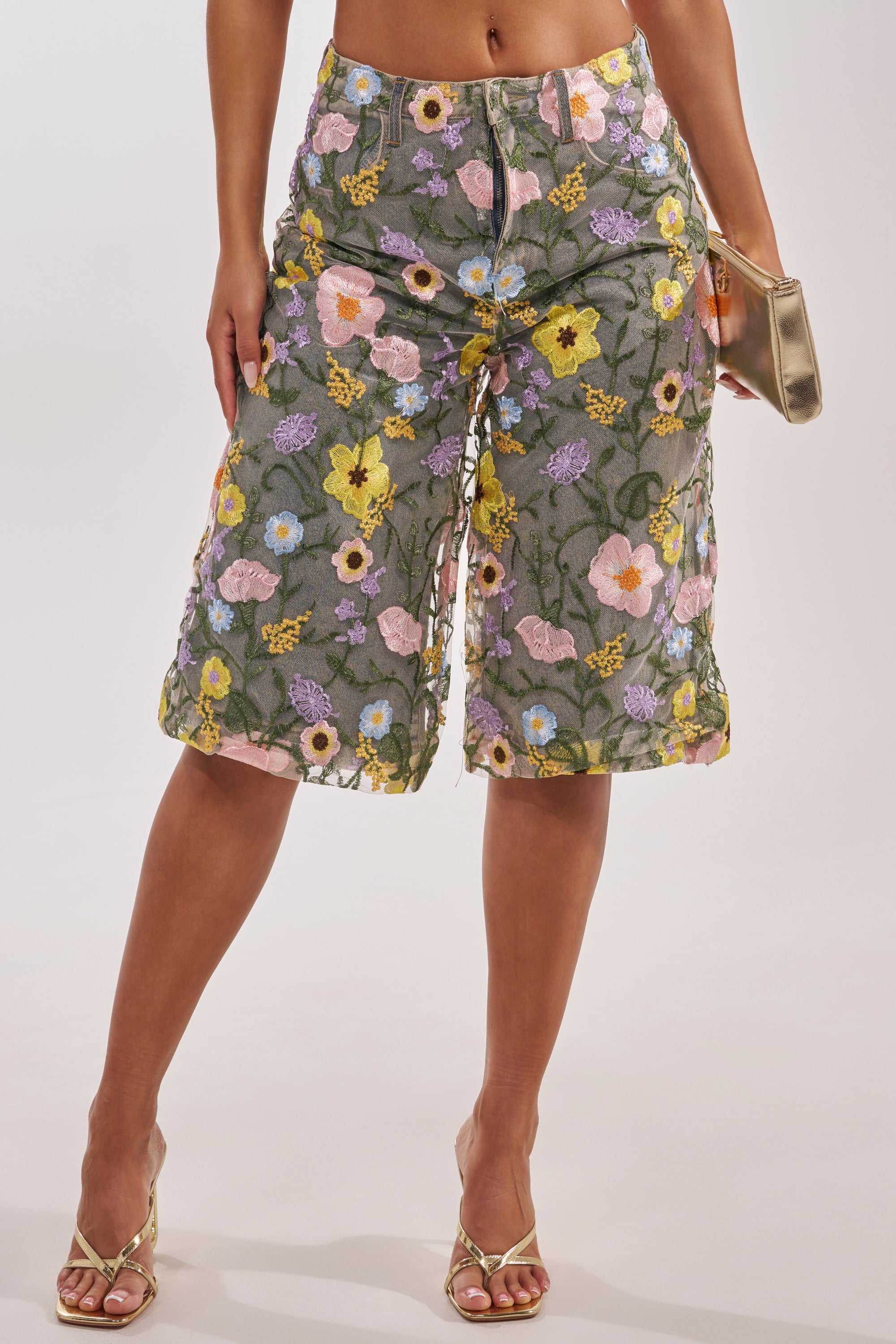 Wearing GARDEN PARTY STRETCH DENIM WITH FLORAL TULLE BERMUDA SHORTS, paired with strappy heeled sandals and a metallic clutch purse. 4
