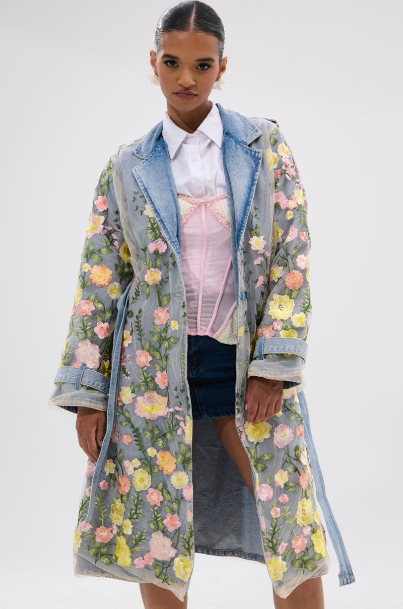 A woman models the LIFE IN COLOR FLORAL DENIM TRENCH with a sheer mesh overlay, styled over a white shirt, pink corset, and dark denim skirt against a plain light background.