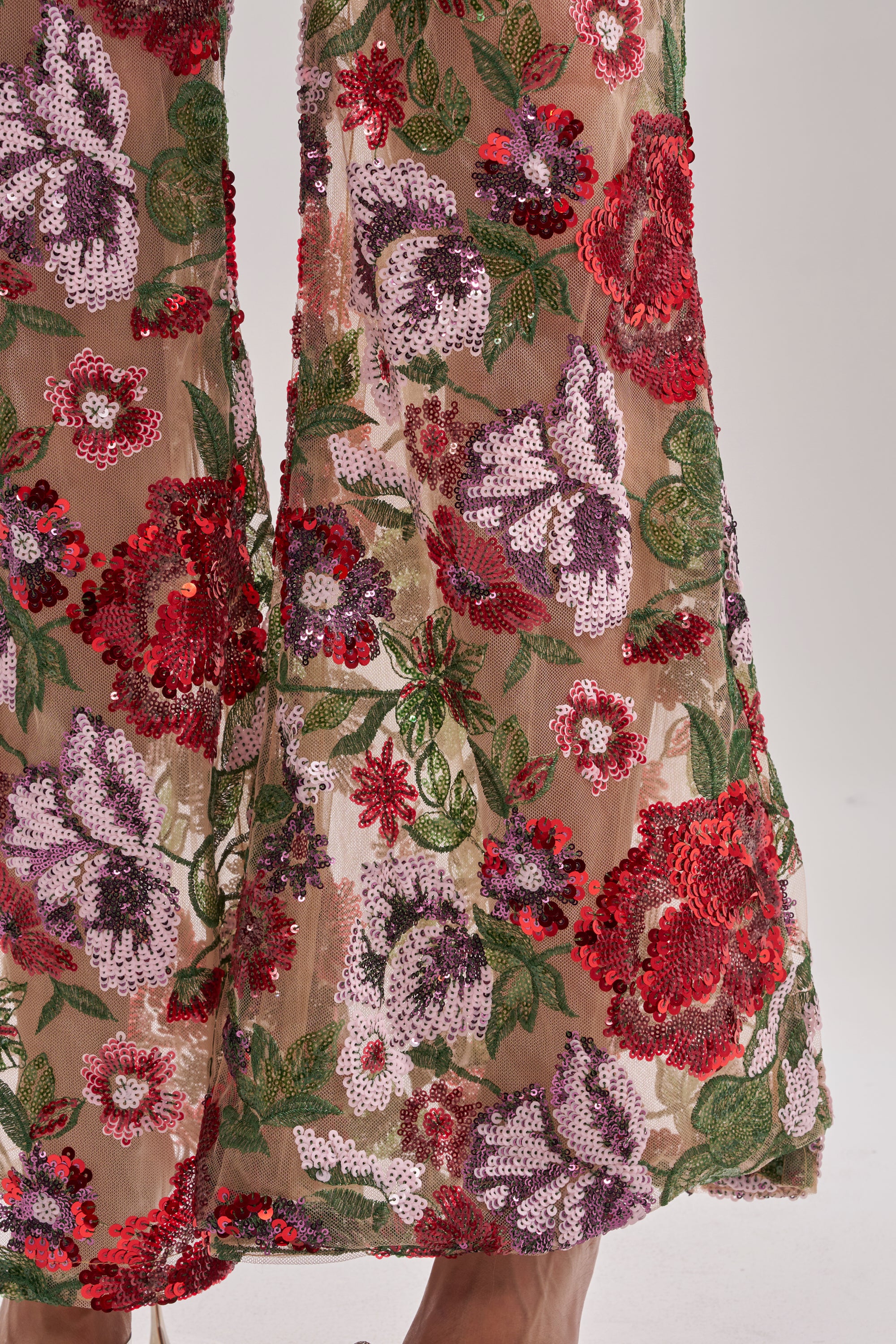 Close-up of ENCHANTED GARDEN FLORAL EMBROIDERED TULLE PANT, showcasing a high-rise flared-leg silhouette with red, purple, and green floral sequin embroidery, intricate patterns, and shimmering details.