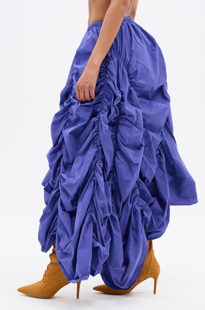 A person wears the NOT ABOUT IT RUCHED MIDI SKIRT with an asymmetrical hem and tan pointed-toe high-heeled boots, shown from the side against a plain white background. 3