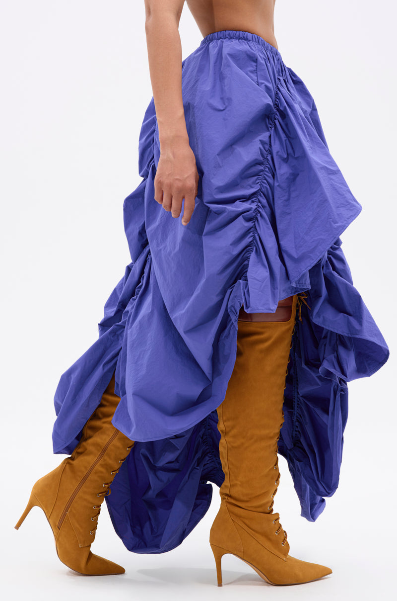 A person wearing the NOT ABOUT IT RUCHED MIDI SKIRT with a voluminous, asymmetrical hem and tan suede lace-up knee-high heeled boots, standing against a plain white background. 4