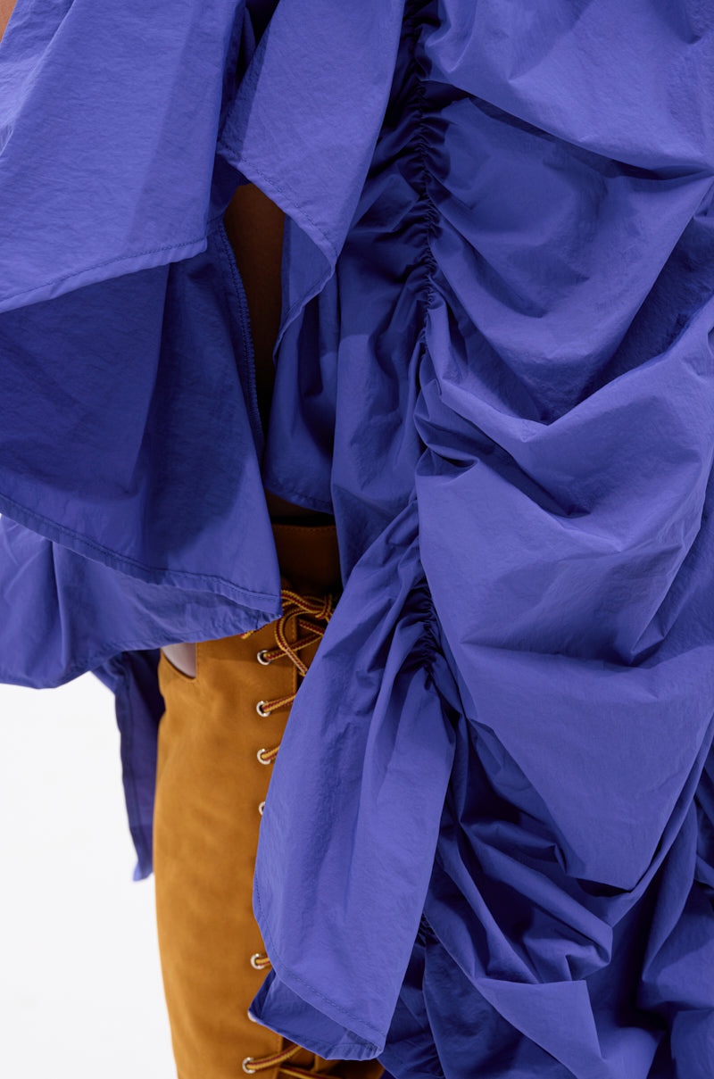 Close-up of a person wearing the NOT ABOUT IT RUCHED MIDI SKIRT in textured blue over mustard-yellow pants with visible lace-up details, set against a plain white background. 6